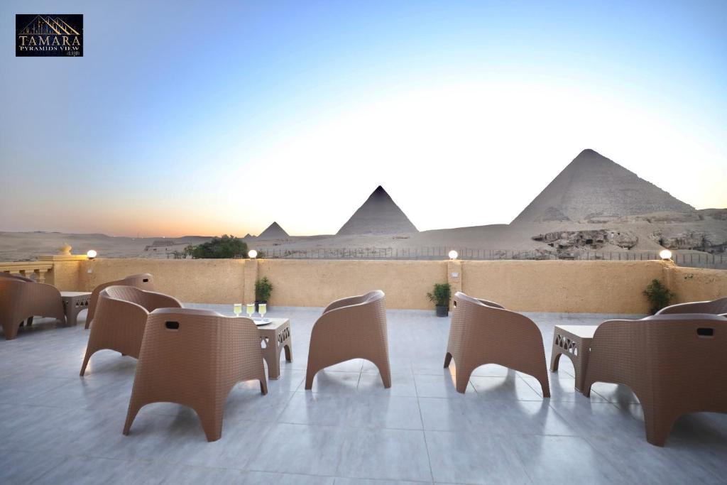 a patio with tables and chairs with pyramids in the background at Tamara Pyramids View in Cairo