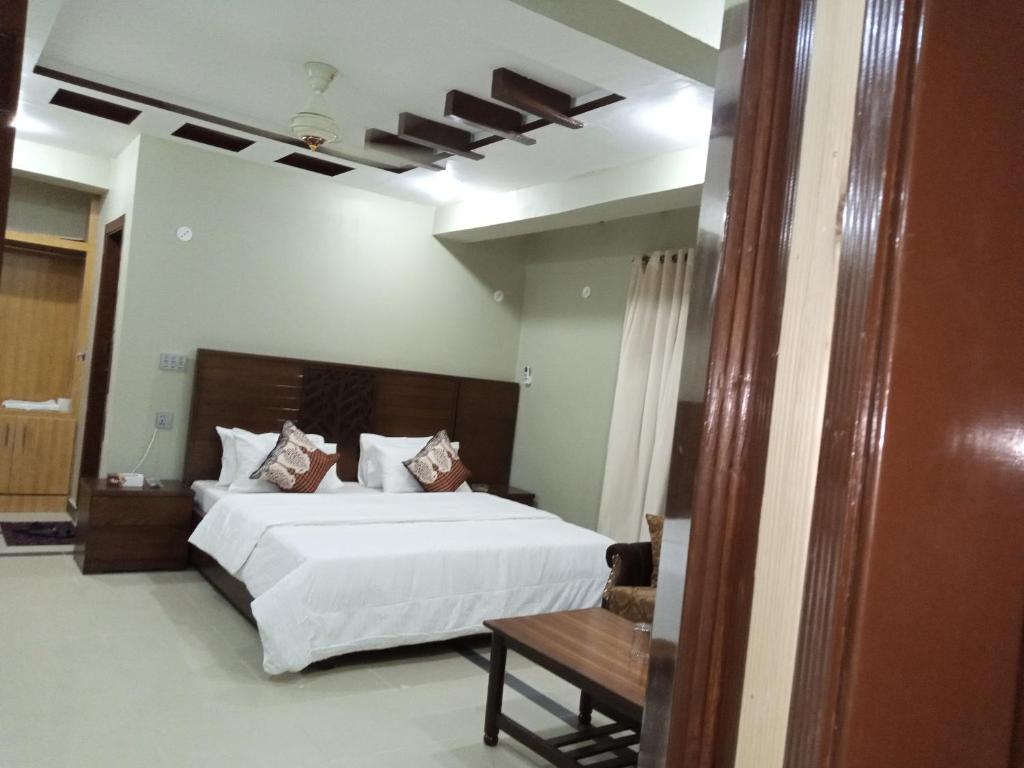 a bedroom with a large white bed and a table at Hotel AL MARKAZ in Islamabad