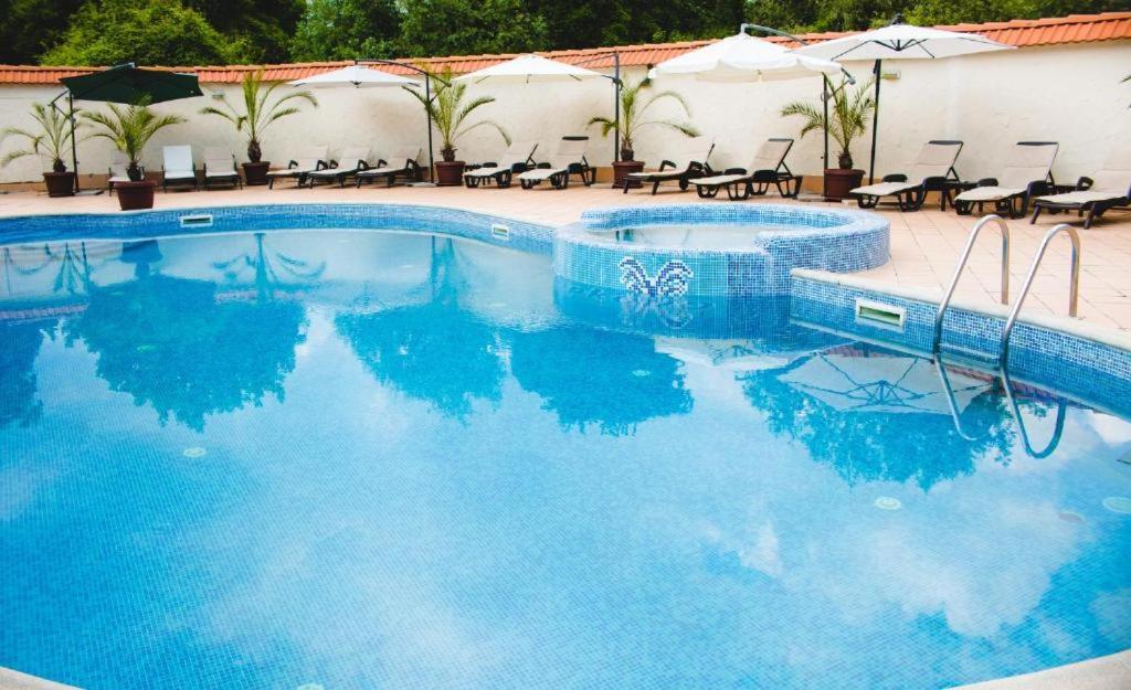 una piscina con agua azul, sillas y sombrillas en Family Hotel Shipkovo, en Shipkovo
