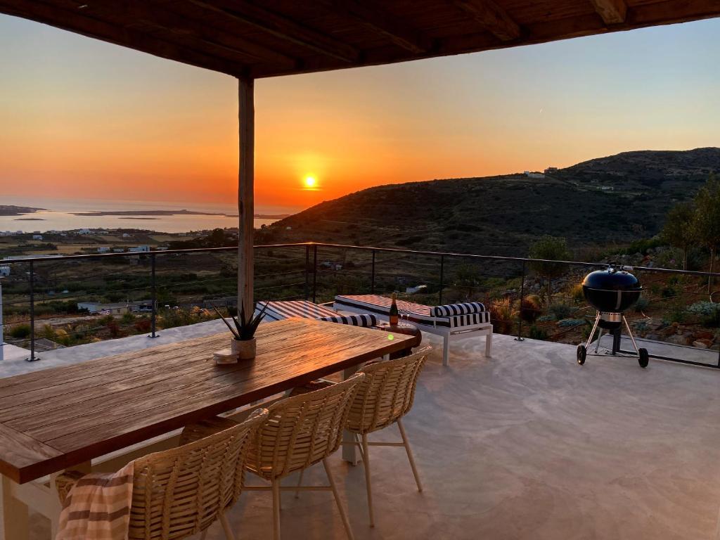 een patio met een houten tafel en stoelen en de zonsondergang bij Sun House Paros in Kampos Paros