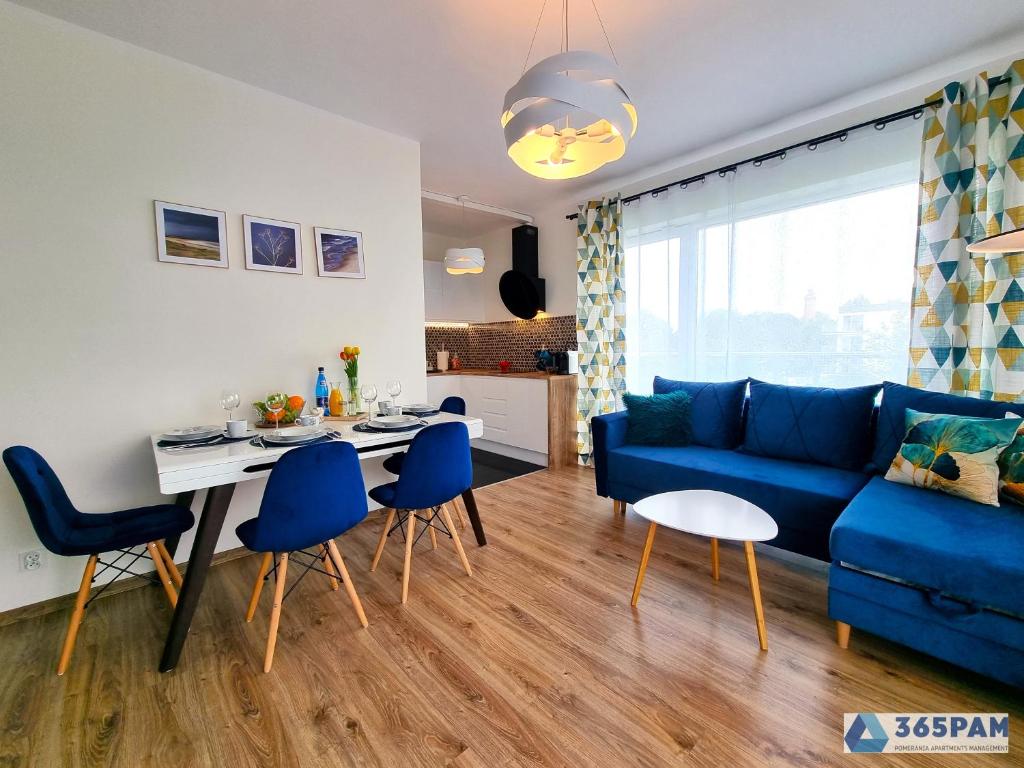 a living room with a blue couch and a table and chairs at Apartamenty Na Fali w Gąskach - 365PAM in Gąski