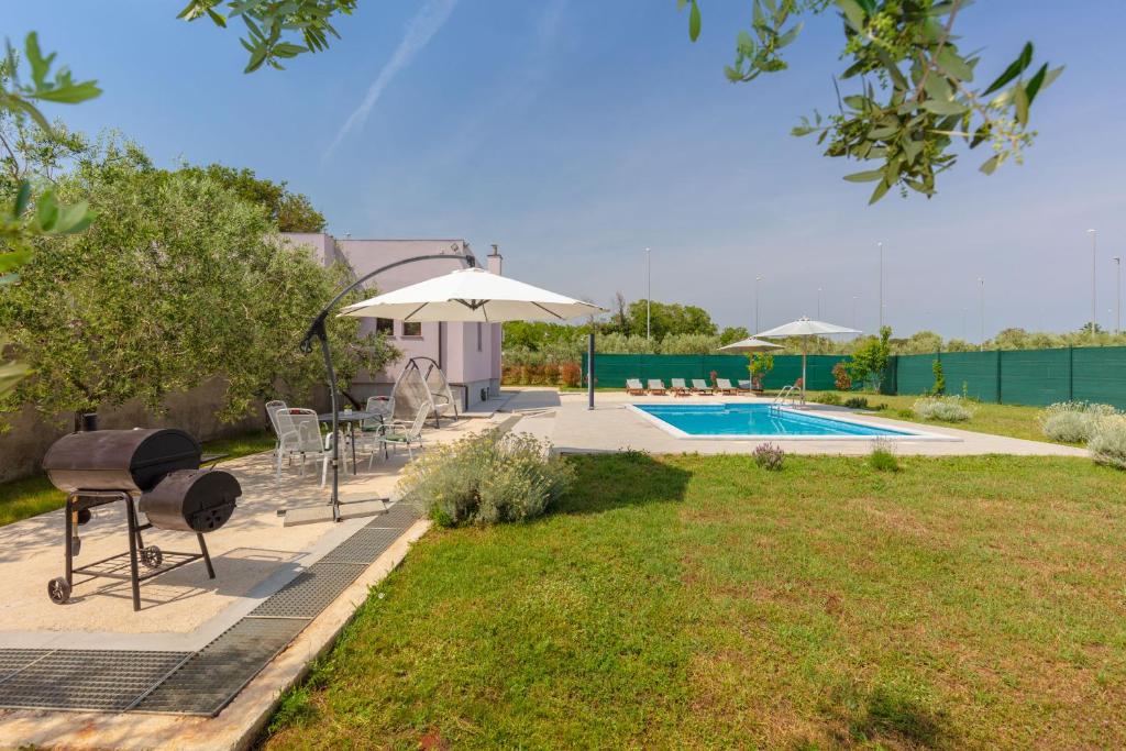 een achtertuin met een zwembad en stoelen en een parasol bij Villa VIOLA with pool, whirlpool, playground & bbq in a olive grove with sea view, near the beach, Pomer - Istria in Pomer