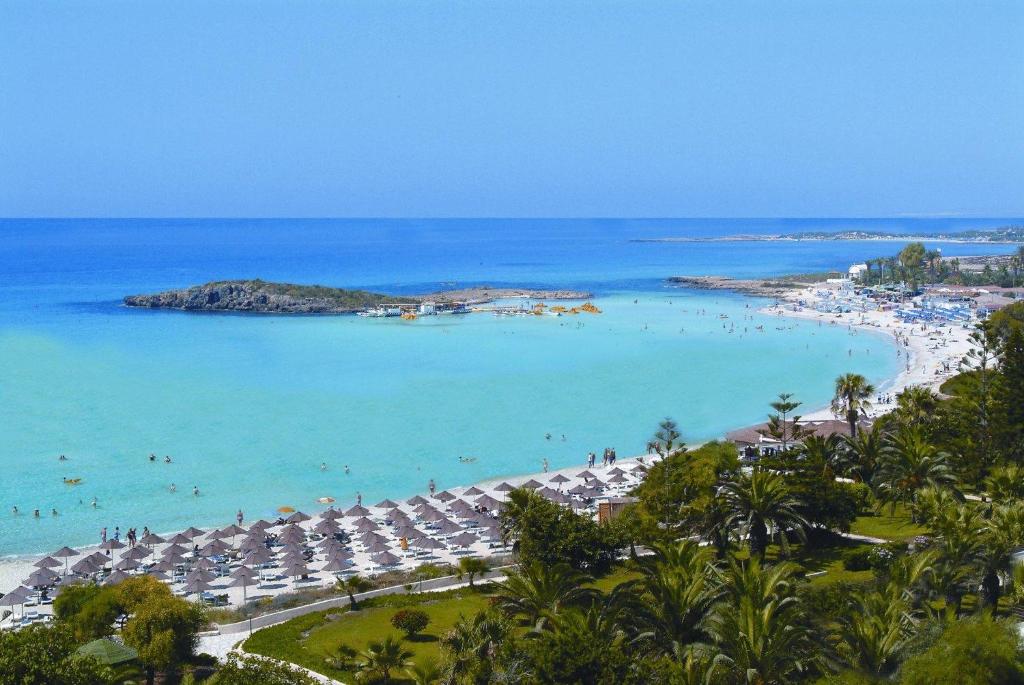 a beach with umbrellas and people in the ocean at Nissiana Hotel & Bungalows in Ayia Napa