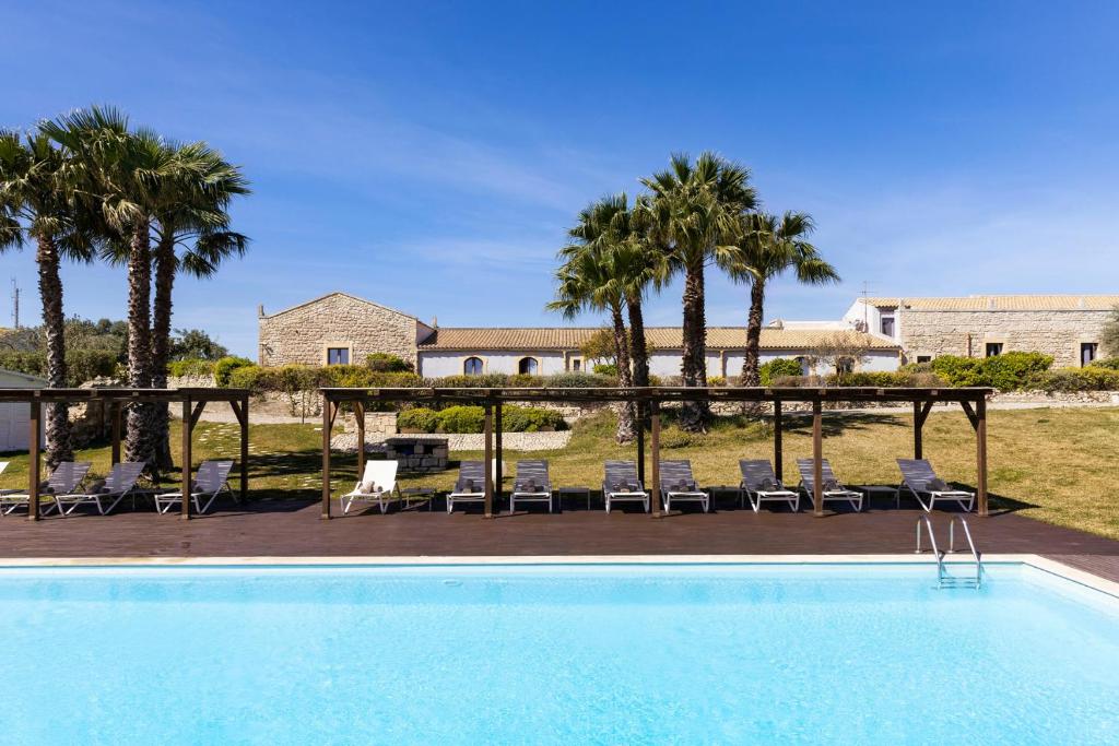 a pool with chairs and a table and palm trees at Masseria del Carrubo in Noto