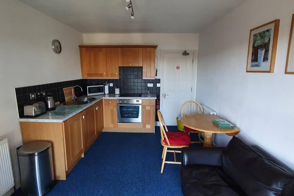 a kitchen with wooden cabinets and a table and a couch at Stylish, comfortable apartment with balcony in Plymouth