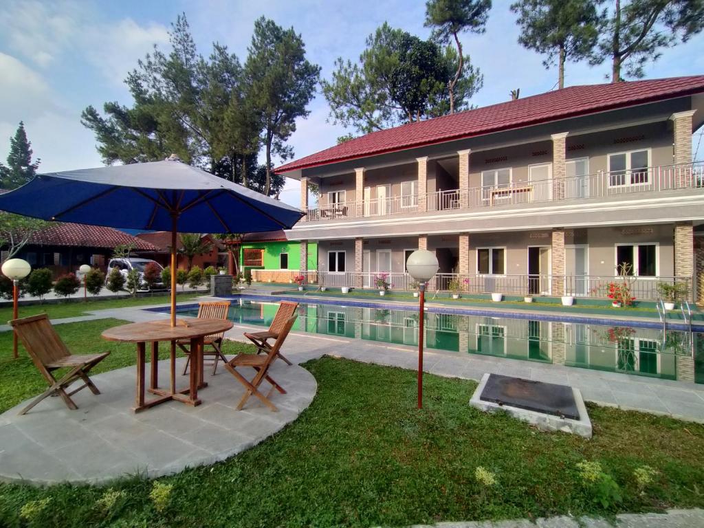 um pátio com uma mesa e guarda-sol ao lado de uma piscina em Villa Batu Tua Puncak Mitra RedDoorz em Bogor
