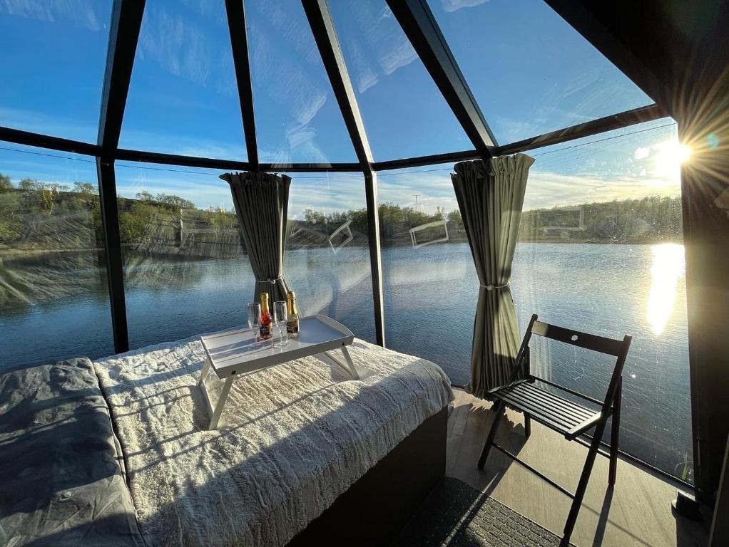 a bedroom with a bed and a chair in front of the water at Aurora Hut - luksusmajoitus iglu tunturilammella Pohjois-Lapissa Nuorgamissa in Nuorgam