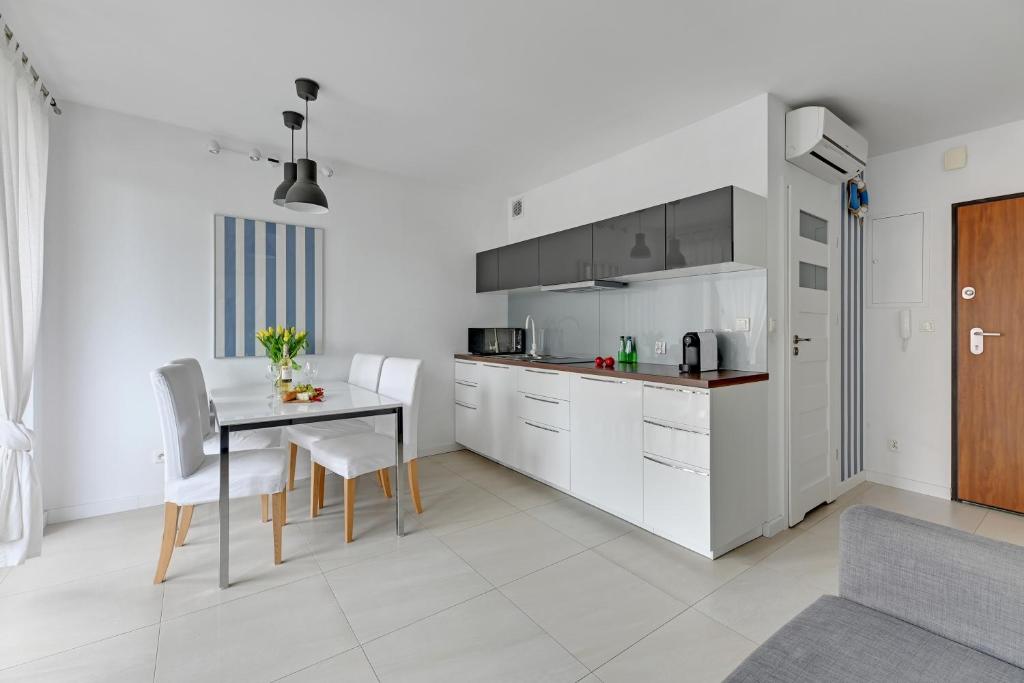 Bright kitchenette and dining area with white cabinets, table set, vases and natural light.