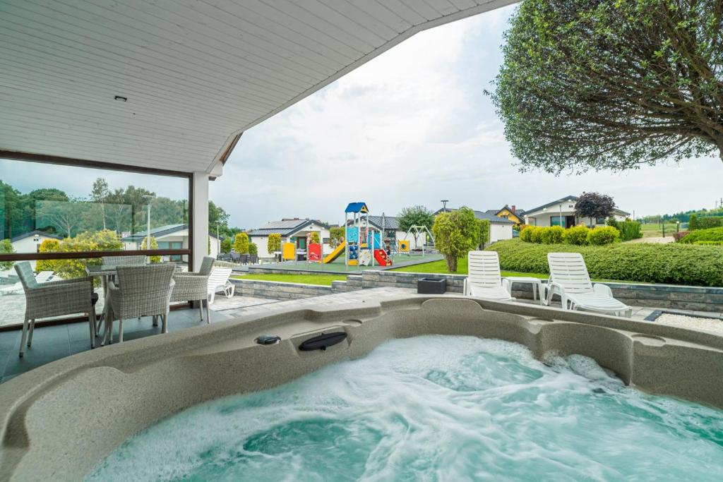 a hot tub in a backyard with chairs and a playground at Duet Domki in Jarosławiec