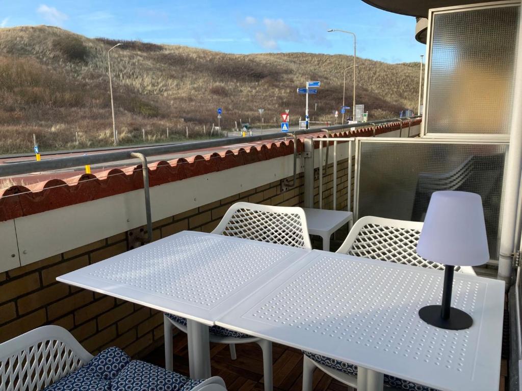 une table et des chaises blanches sur un balcon avec une autoroute dans l'établissement CallantsDuinzicht, Beachappartement 24, à Callantsoog