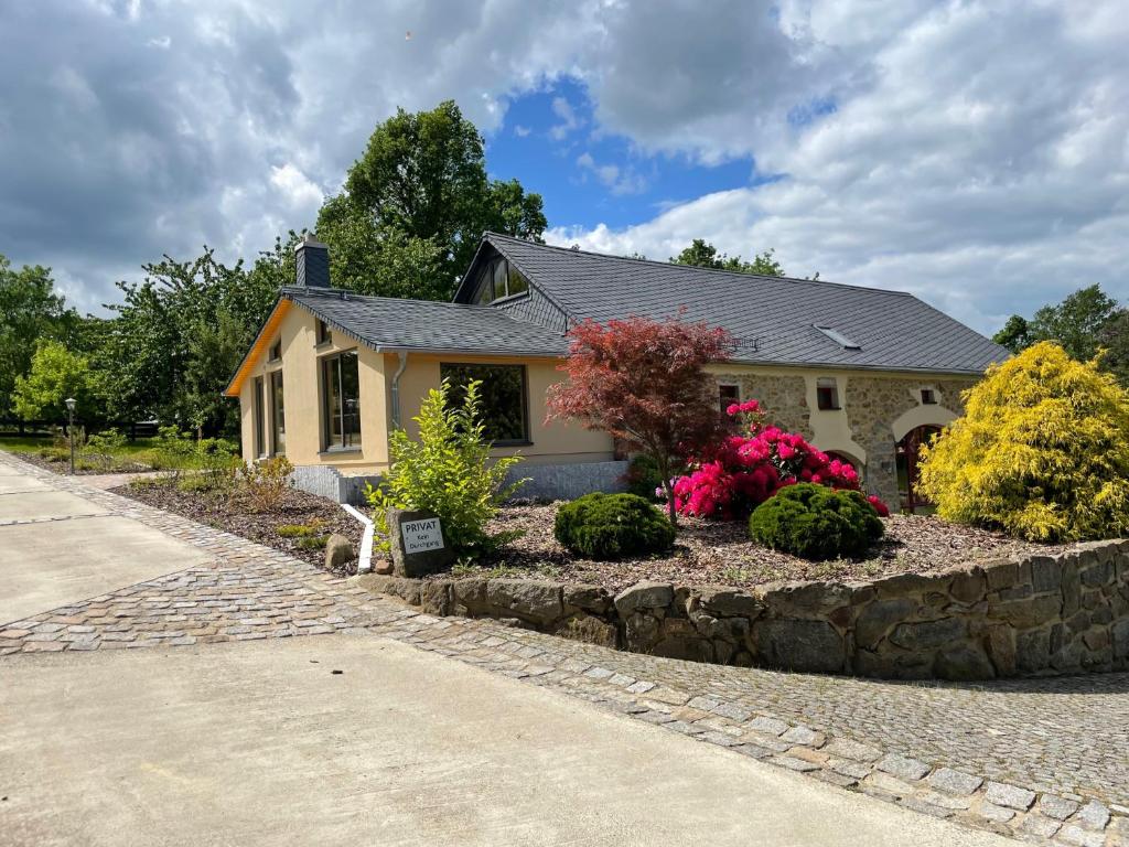 a house with a stone retaining wall in front of a yard at Ferienwohnung-Ferienhaus am Picho in Arnsdorf