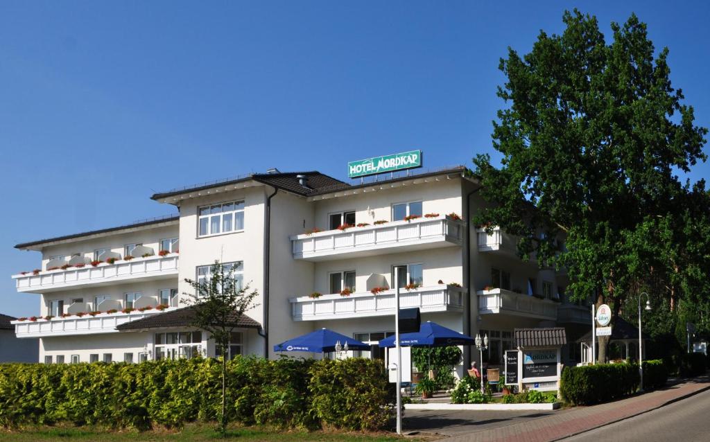 ein weißes Hotel mit blauen Sonnenschirmen davor in der Unterkunft Hotel Nordkap in Ostseebad Karlshagen