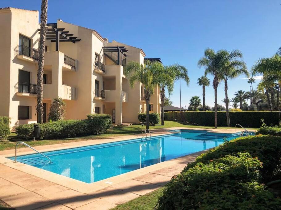 a swimming pool in front of a building with palm trees at Roda Golf Resort ;Casa Sylva in San Javier