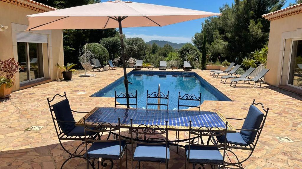 a table and chairs with an umbrella next to a pool at Maison d'Hotes Le Boulou in Saint-Cyr-sur-Mer