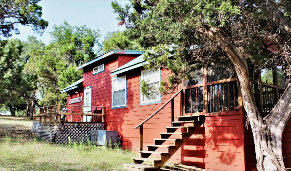 a red house with a deck next to a tree at HomeAway Cabins and Animal Sanctuary in Boerne