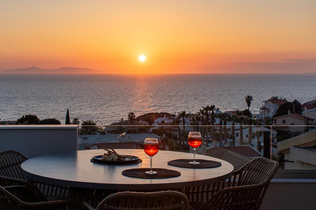 a table with two glasses of wine on a balcony with the sunset at LazySun in Sounio