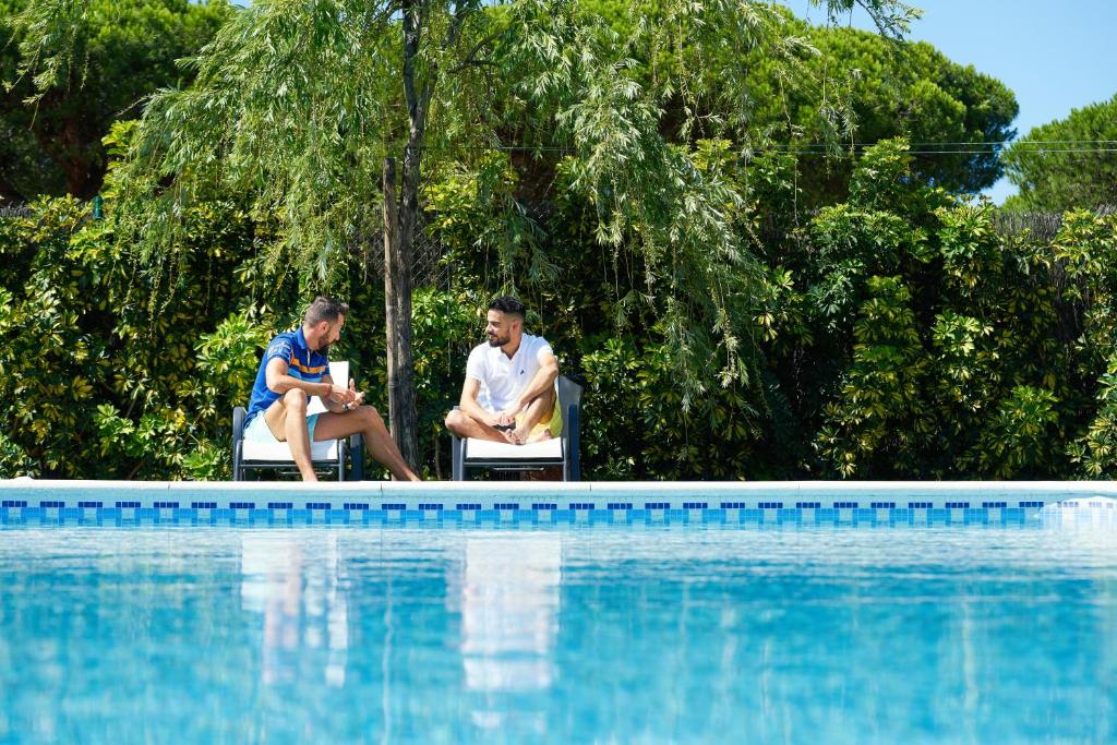 two men sitting in chairs next to a swimming pool at Hotel Albaida Nature in Mazagón