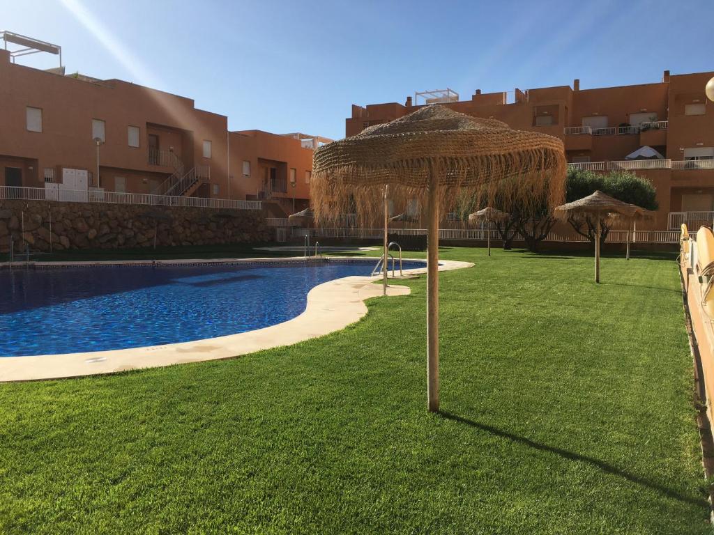 a large straw umbrella in the grass next to a swimming pool at Las Brisas Mojacar Home in Mojácar