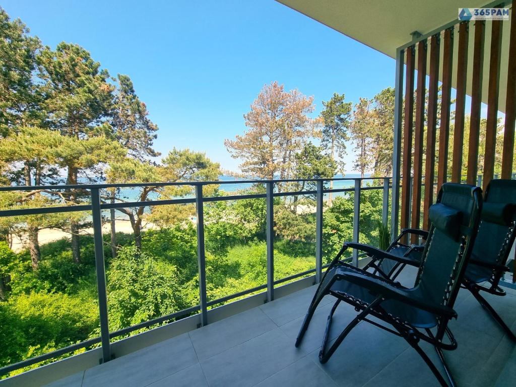 2 sillas en un balcón con vistas a los árboles en Apartament LET'S SEA z widokiem na morze - 365PAM, en Gąski