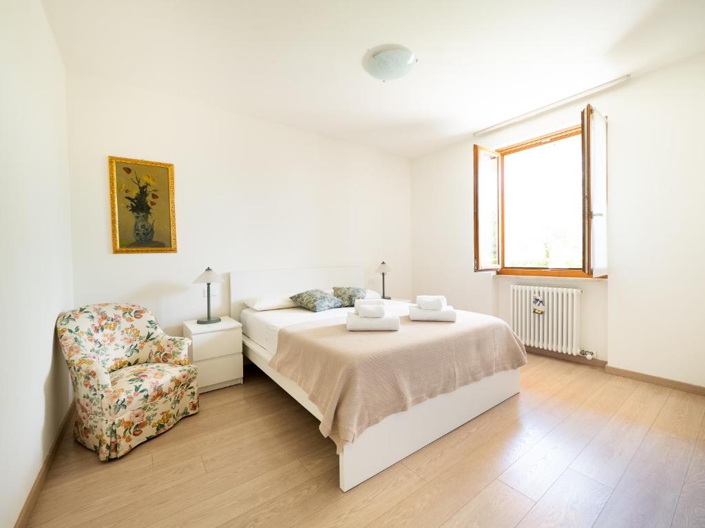 een witte slaapkamer met een bed en een stoel bij Luminosa casetta per due in Bardolino