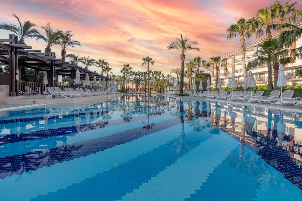 einen Hotelpool mit Palmen und Sonnenuntergang in der Unterkunft Belek Beach Resort Hotel in Belek