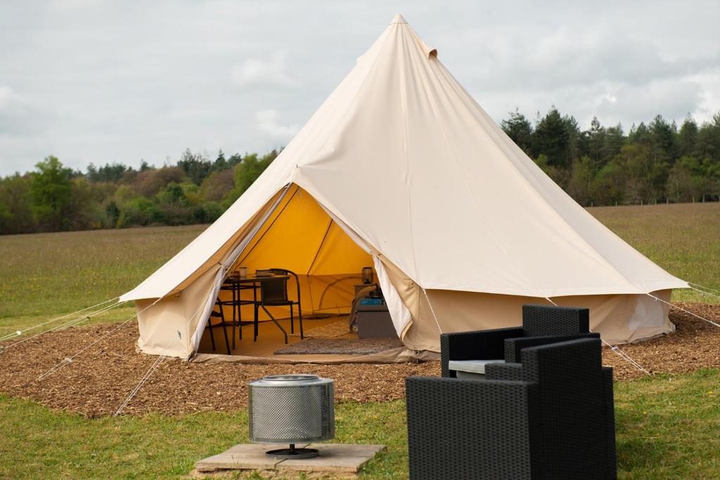 a tent with a table and chairs in a field at Forest Edge Glamping in Gittisham