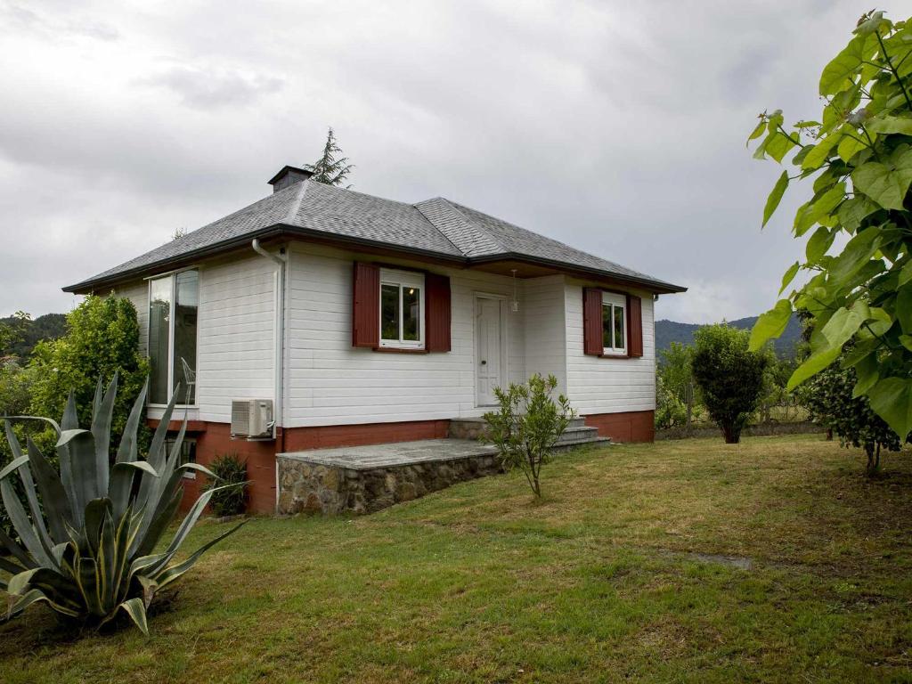 una pequeña casa blanca con adornos rojos en un patio en A Casiña Casa Rural en Galicia, en Ourense