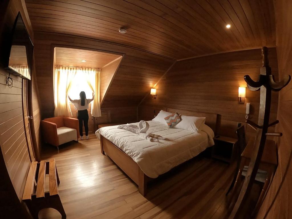 Un dormitorio con una cama y una persona parada en una ventana en Hotel Heidinger en Oxapampa