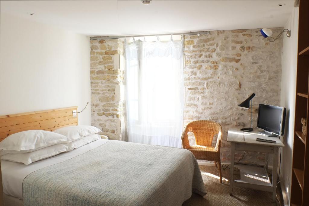 a bedroom with a bed and a desk with a television at Hôtel Le Sénéchal in Ars-en-Ré