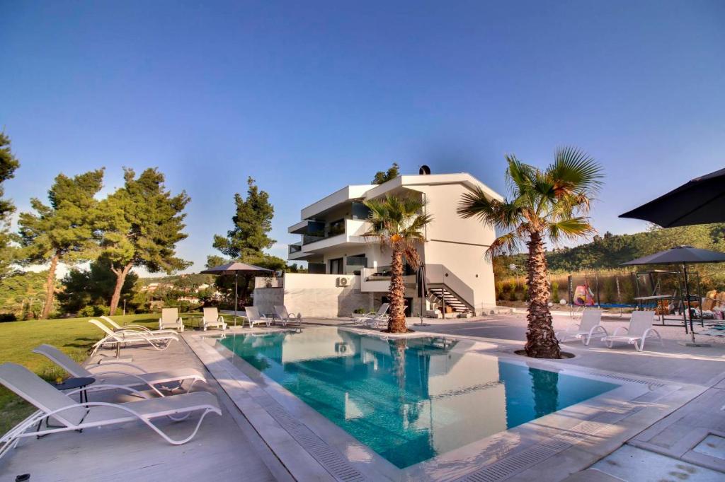 a swimming pool with chairs and palm trees in front of a house at Pine Resort in Polykhrono