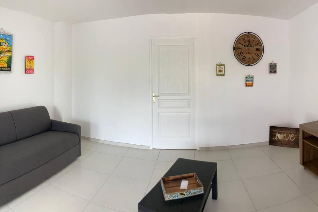 ein Wohnzimmer mit einem Sofa und einer Uhr an der Wand in der Unterkunft KAZ'ANTILLAISE APPT AVEC PISCINE TI MAEVA 3/4P. LE LAMENTIN in Le Lamentin