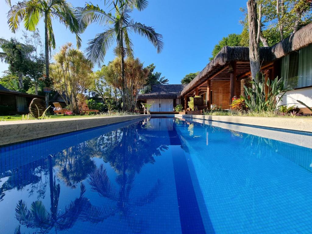 a swimming pool in front of a house with palm trees at Villa Bulan in Arraial d'Ajuda