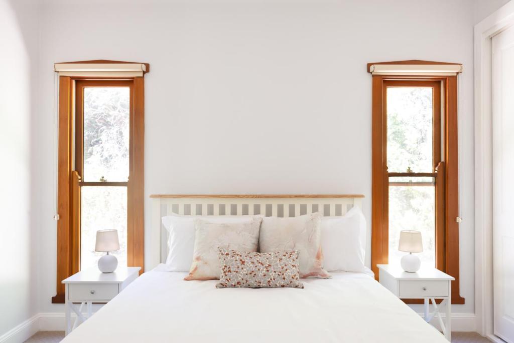 a white bedroom with a large white bed with two windows at Kuzman Homestead in Mudgee
