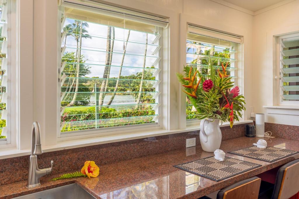 a kitchen with two windows and a sink with flowers at Fern Grotto Inn in Kapaa