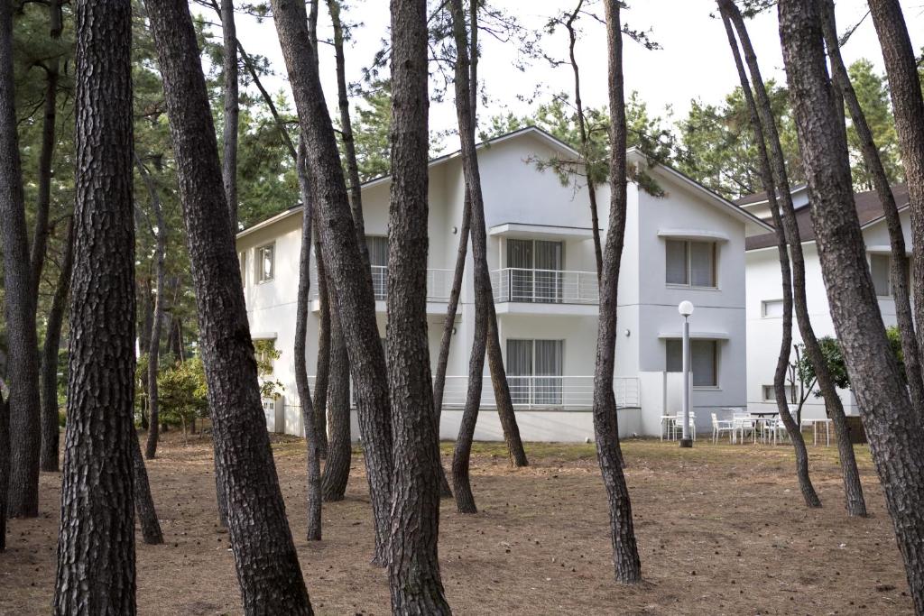 uma casa branca atrás de uma floresta de árvores em Luxze Hitotsuba/Cottage Himuka em Miyazaki