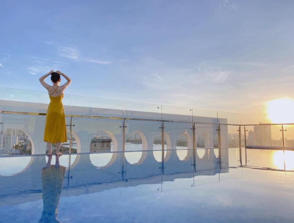 A rooftop pool terrace catches the sunset behind a guest in a yellow dress.