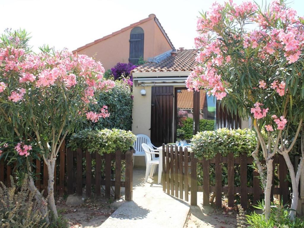 uma cerca em frente a uma casa com flores cor-de-rosa em Maison Gruissan, 1 pièce, 4 personnes - FR-1-229-54 em Gruissan