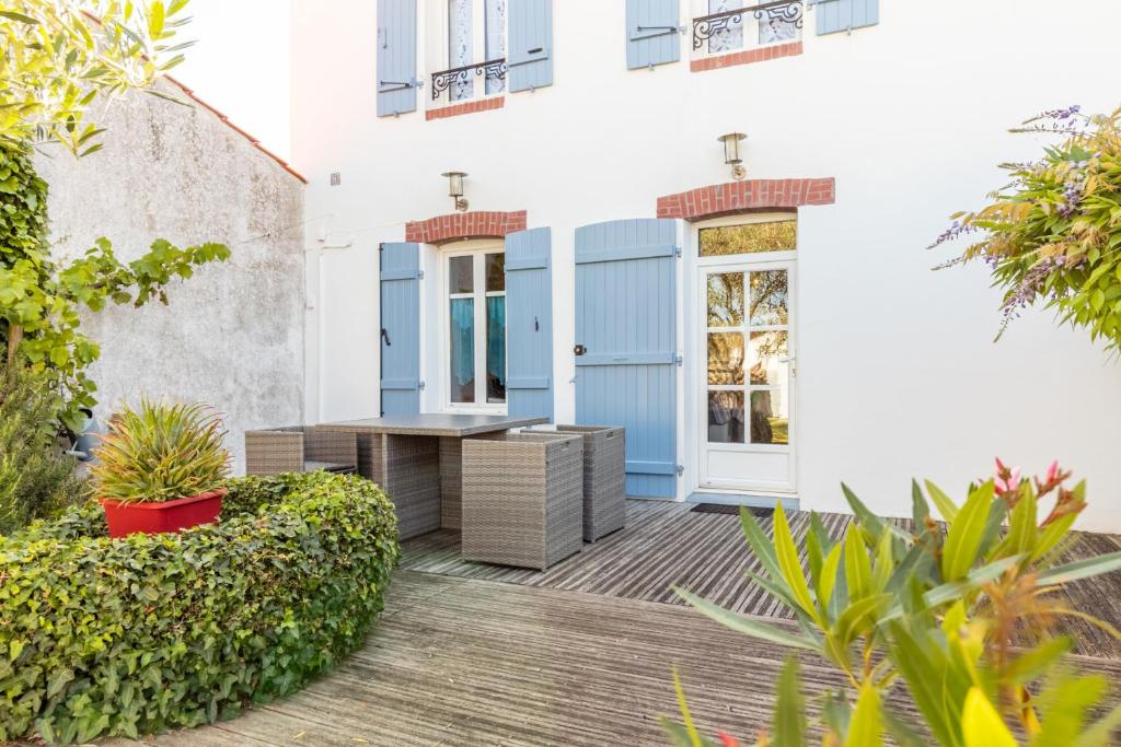 ein weißes Gebäude mit blauen Türen und einer Holzterrasse in der Unterkunft Une maison de charme avec jardin sur l’île de Noirmoutier in LʼÉpine