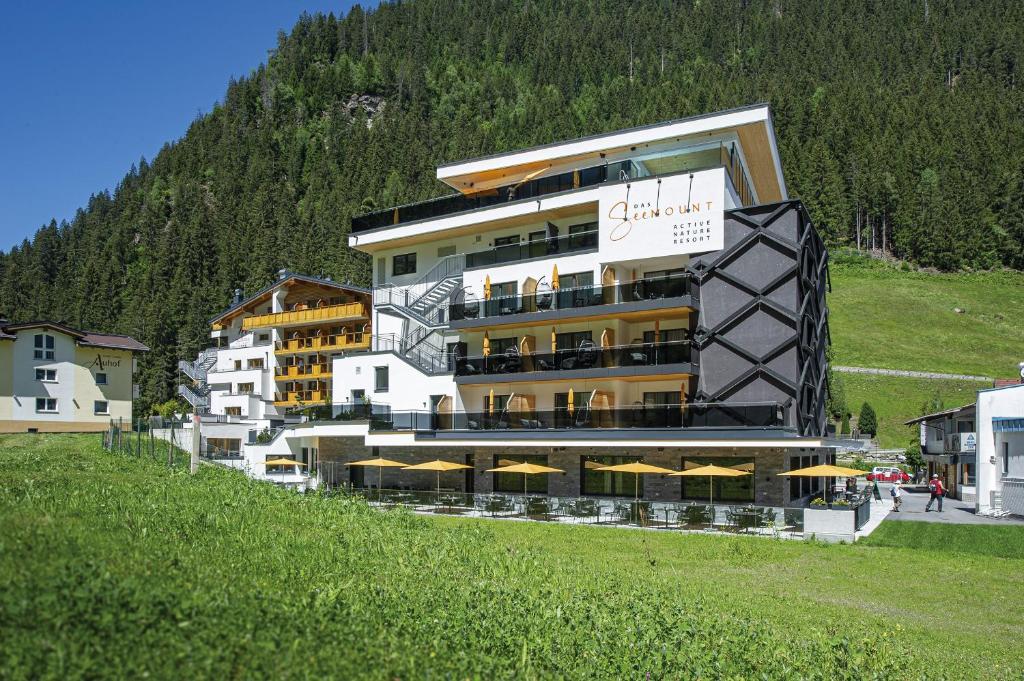 a large building with yellow umbrellas in front of a mountain at Active Nature Resort DAS SeeMOUNT in See