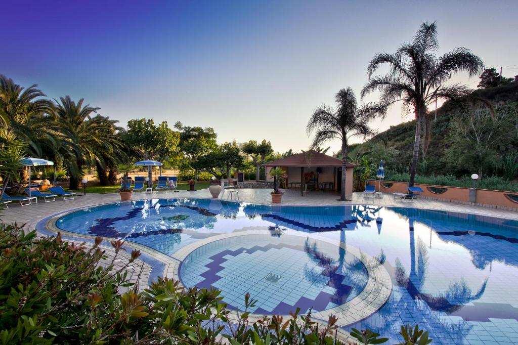 een groot zwembad met blauw water en palmbomen bij Hotel Villaggio Old River in Capo Vaticano