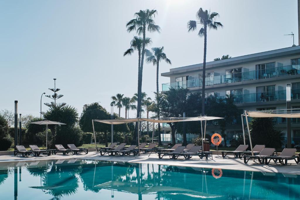 a hotel room with a pool and lawn chairs at Helios Mallorca Hotel & Apartments in Can Pastilla