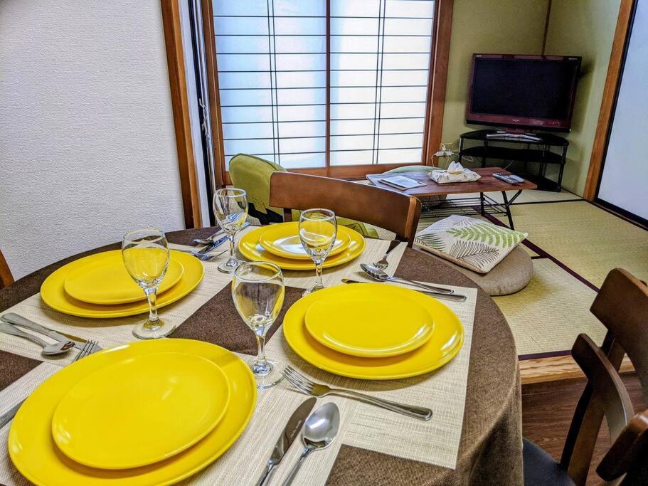 a dining room table with yellow plates and wine glasses at Oiwake House 1B in Karuizawa