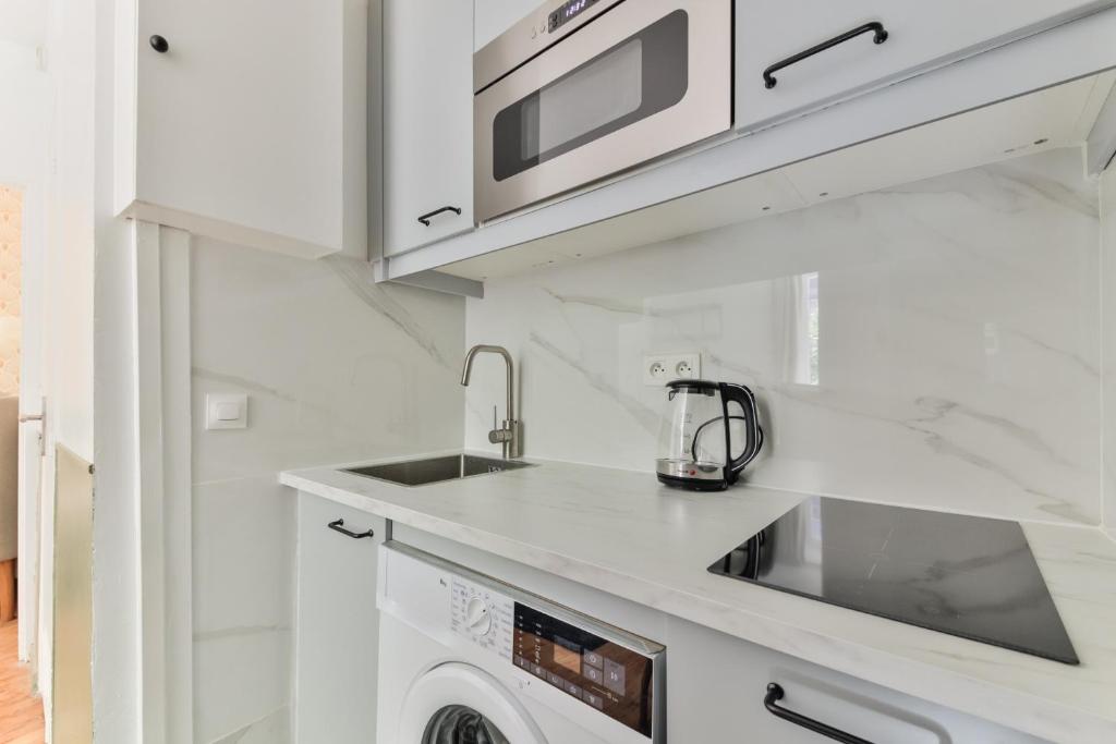 a white kitchen with a sink and a microwave at indépendant flat: canal st martin&amp;trains stations! in Paris