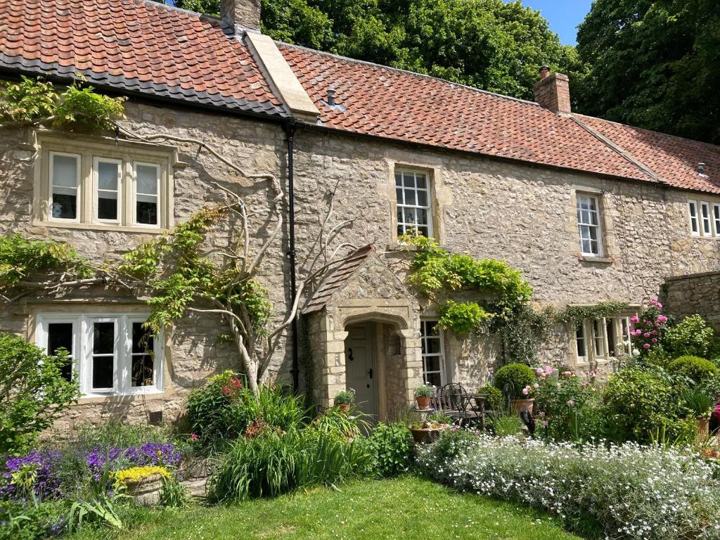 une vieille maison en pierre avec des fleurs dans la cour dans l'établissement Maplestone, à Shepton Mallet