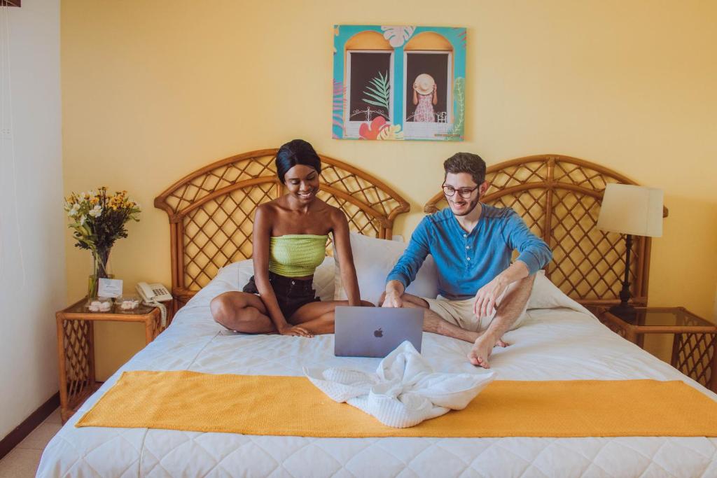un uomo e una donna seduti su un letto con un portatile di Hotel Santana a Flores