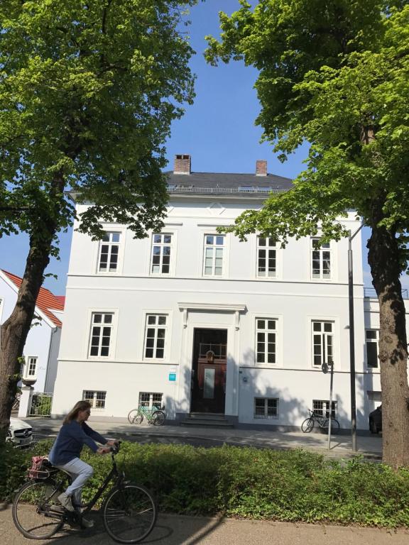 a woman riding a bike in front of a white building at Tresor am Staatstheater in Oldenburg