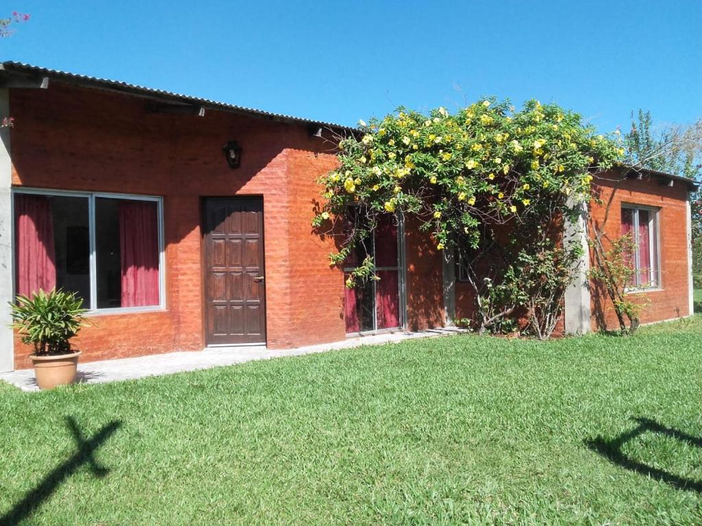 a brick house with a door and a green yard at Cabaña Aguara in Colonia Carlos Pellegrini