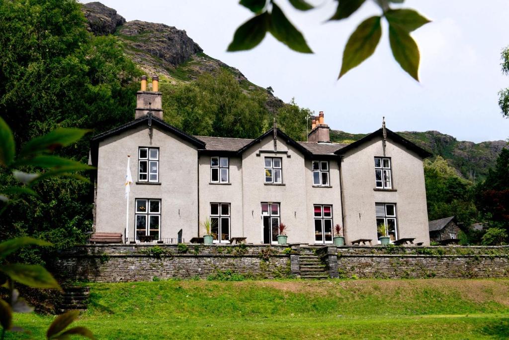 una gran casa blanca con una colina en el fondo en YHA Coniston Holly How en Coniston