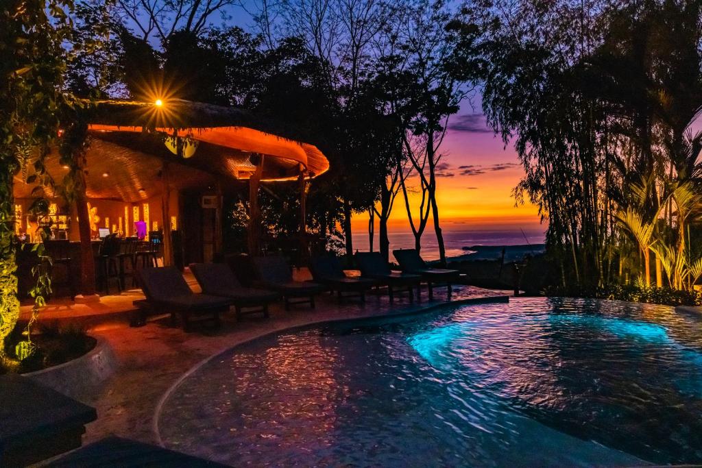 ein Pool mit Stühlen und ein Sonnenuntergang im Hintergrund in der Unterkunft Selva Armonia Immersive Jungle Resort in Uvita