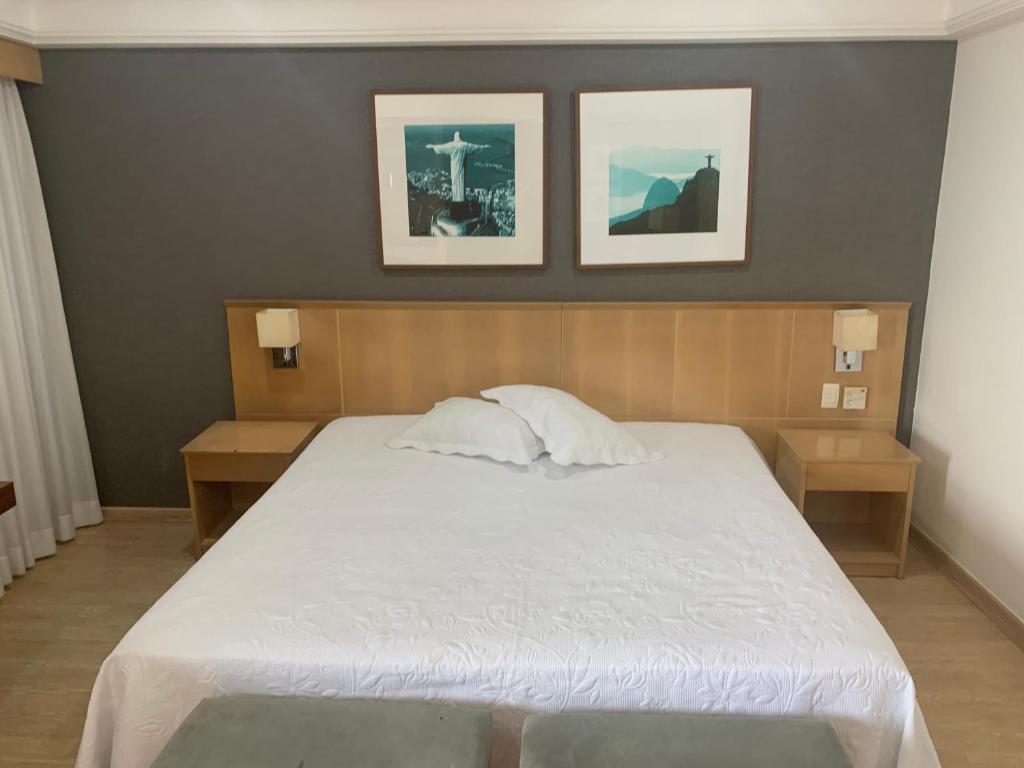 a bedroom with a large white bed with two tables at Lindo Flat na Barra da Tijuca com vista para o mar in Rio de Janeiro